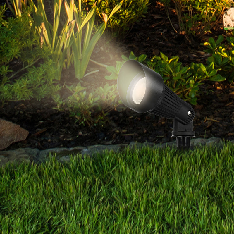 Garden light fixture illuminating a grassy area with plants in the background