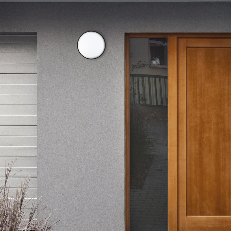 Round outdoor light fixture on a gray wall next to a wooden door.