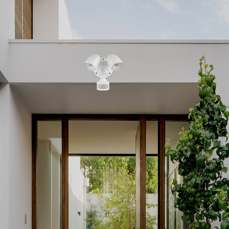 White outdoor security camera on a modern building exterior with a view of greenery.