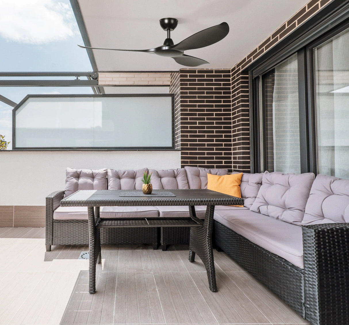 IP55 rated ceiling fan suitable for fully installations Outdoor patio with gray wicker furniture, table, and ceiling fan.