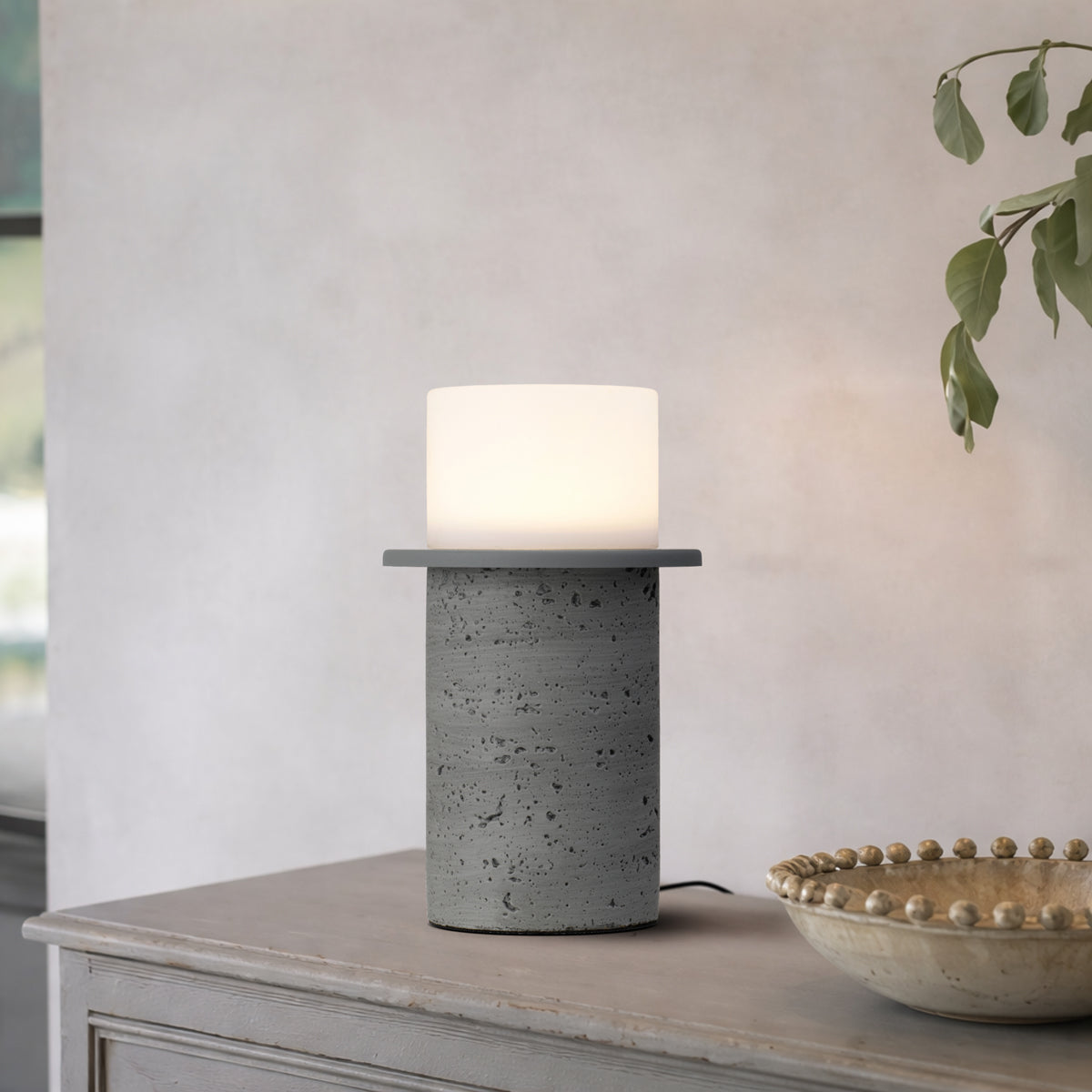 Table lamp with concrete base on a wooden surface, with a plant in the background.