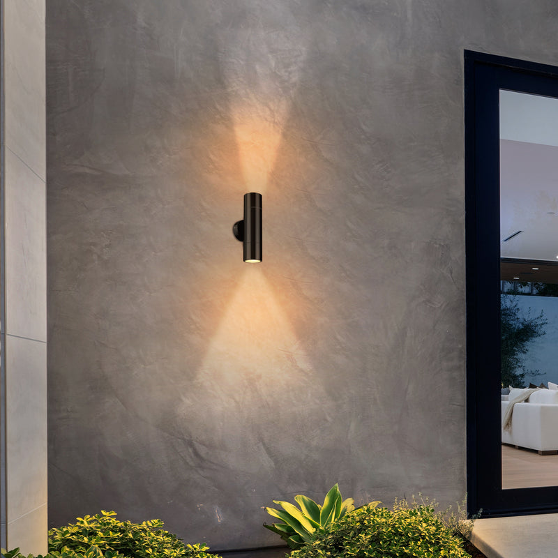 Modern outdoor wall light fixture on a textured concrete wall with plants in the foreground.