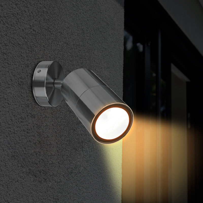 Chrome wall-mounted outdoor light fixture on a dark wall with a warm glow.