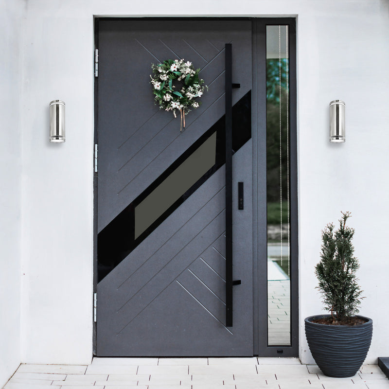 Modern gray front door with decorative wreath and plant on a white wall.