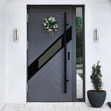 Modern gray front door with decorative wreath and plant on a white wall.
