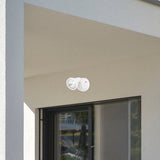 Two white circular light fixtures on a beige wall next to a window.